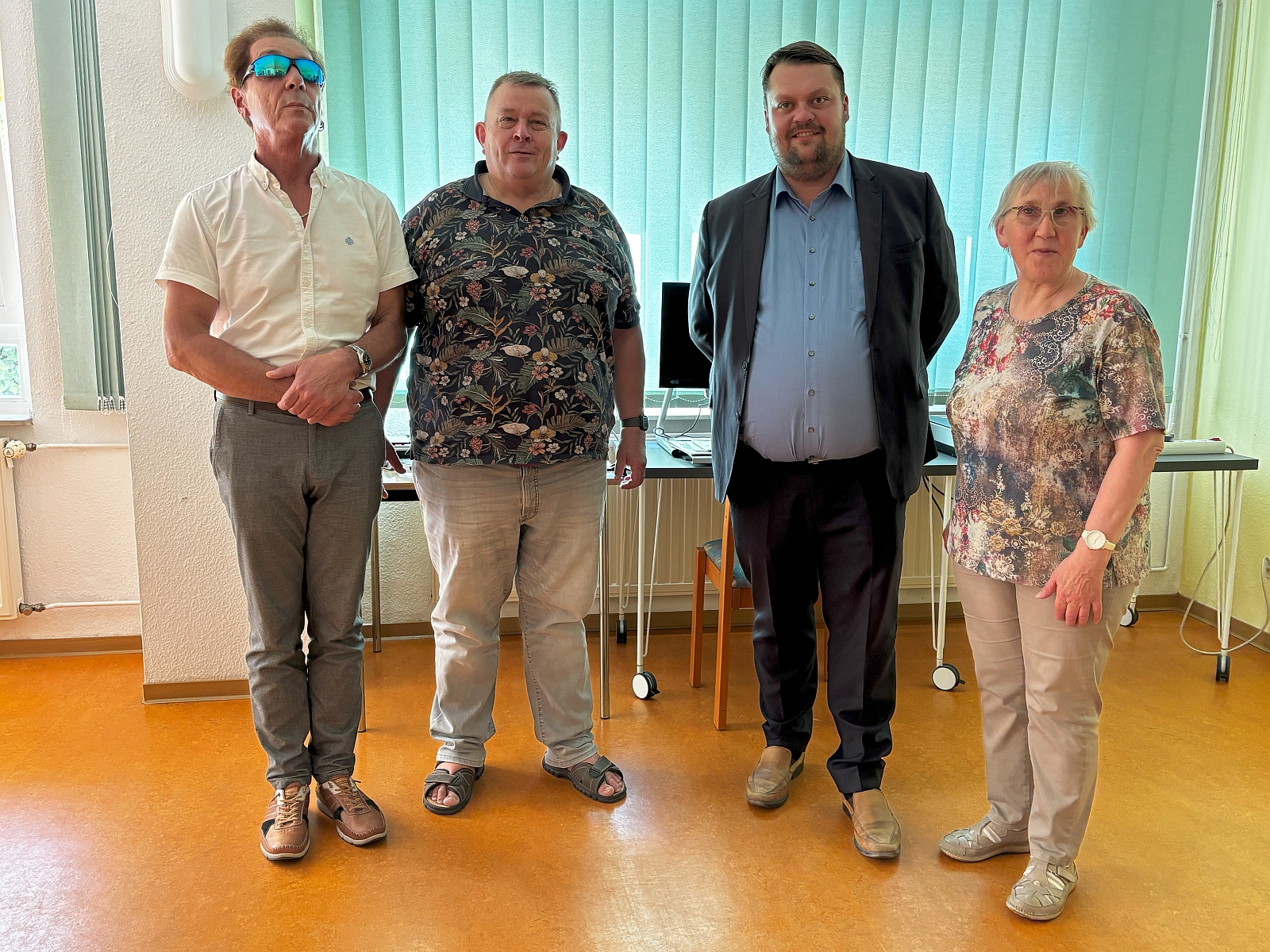 Vier Personen stehen nebeneinander in einem Raum mit Computern.